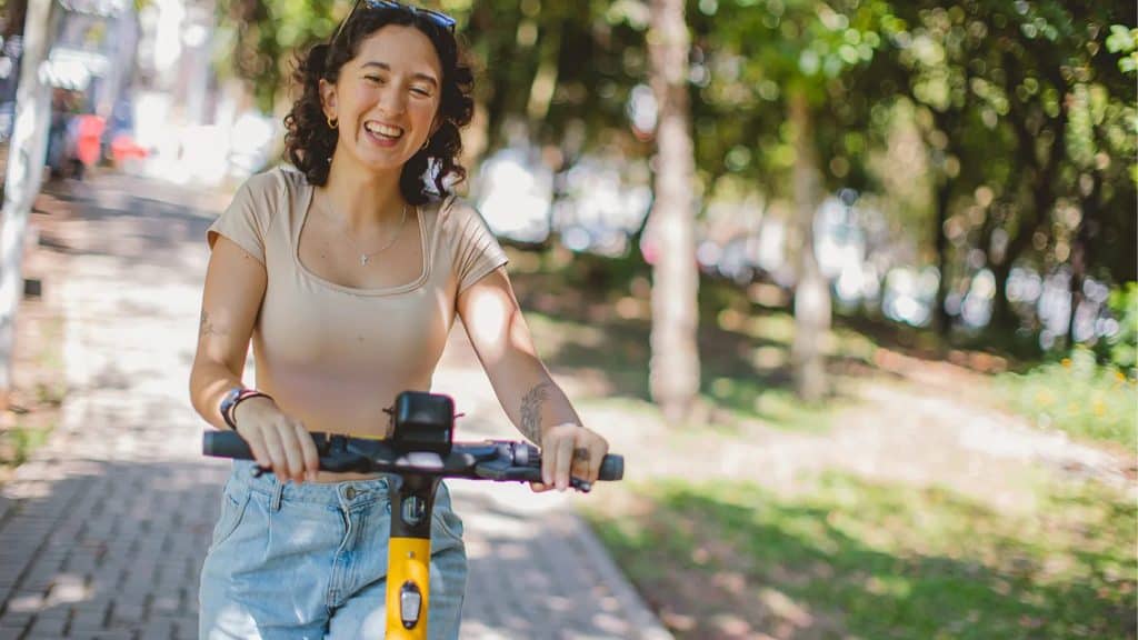 Moça sorrindo enquanto conduz uma das patinetes elétricas da Whoosh