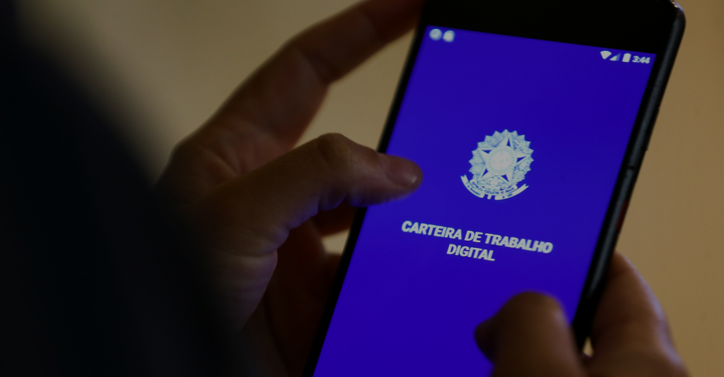 Mãos segurando celular. Tela do celular mostra a carteira de trabalho digital brasileira.