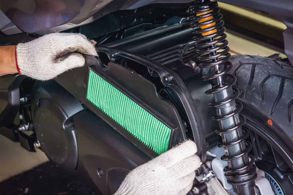 Imagem mostra mãos com luvas instalando  filtro de ar em moto. Conceito de manutenção, serviço e reparo de motocicletas