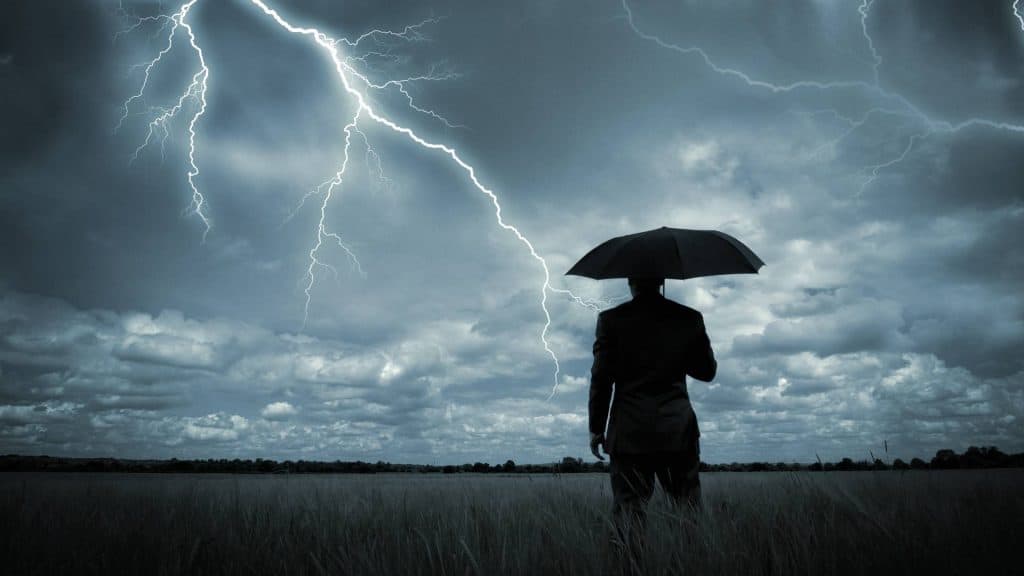 Homem segurando um guarda-chuva observando o céu com nuvens e raios