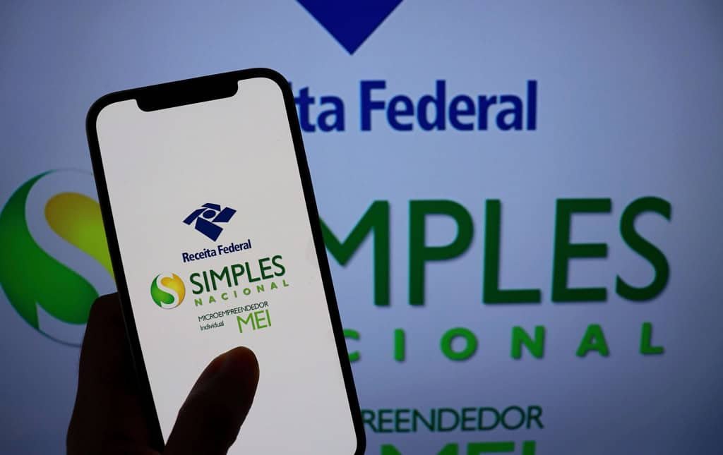 Celular com o aplicativo do Simples Nacional sobre uma tela da Receita Federal.