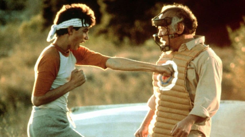 Imagem mostra o personagem de Ralph Macchio dando um soco no personagem de Pat Morita no filme "Karatê Kid: A Hora da Verdade (1984)"