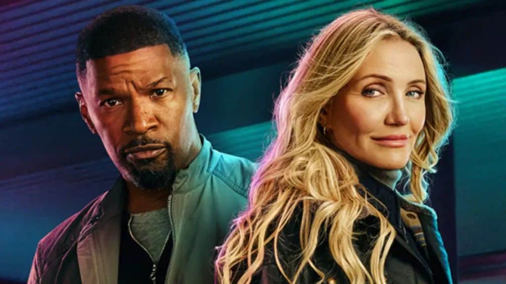 Jamie Foxx e Cameron Diaz estão lado a lado. Ele veste uma jaqueta cinza e olha seriamente para a câmera, enquanto ela, com cabelos loiros soltos e jaqueta preta, sorri levemente. O fundo tem luzes em tons azulados e roxos.