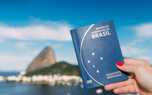 pessoa segurando passaporte brasileiro com o pão de açucar no fundo